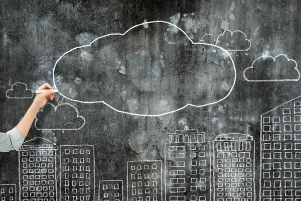 Woman hand holding chalk drawing clouds city buildings — Stock fotografie