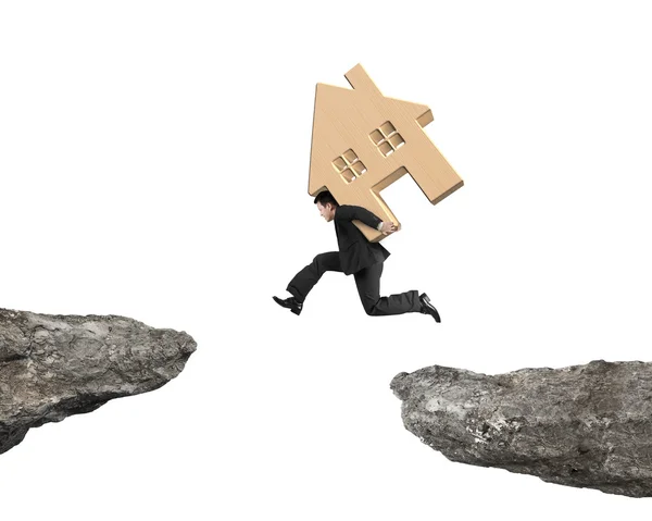 Man carrying wooden house jumping over two cliffs — Stock Photo, Image