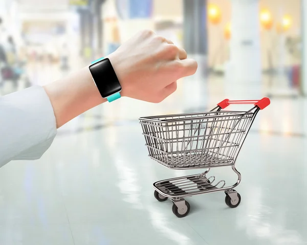 Mão usando relógio inteligente com carrinho de compras pequeno — Fotografia de Stock