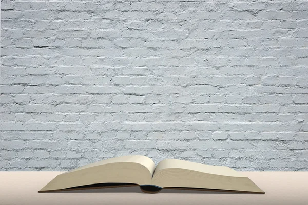 Open book on wooden table with brick wall background — Stock Photo, Image