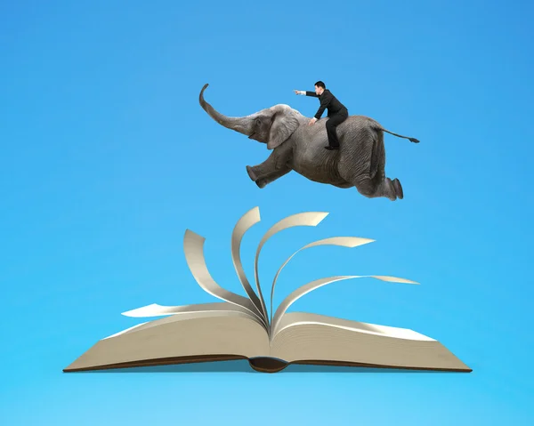 Man riding elephant flying on top flipping pages of open book is — Stock Photo, Image