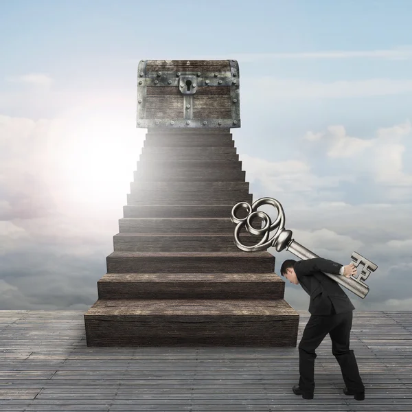 Man carrying key toward treasure chest on wood stairs — Stock Photo, Image