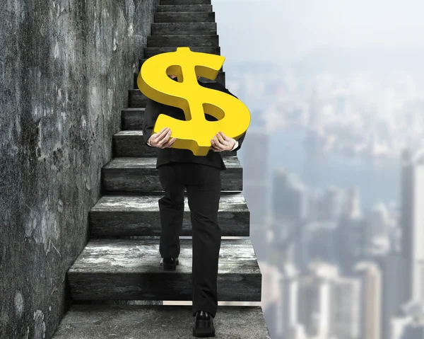 Man carrying golden dollar sign climbing old concrete stairs — Stock Photo, Image