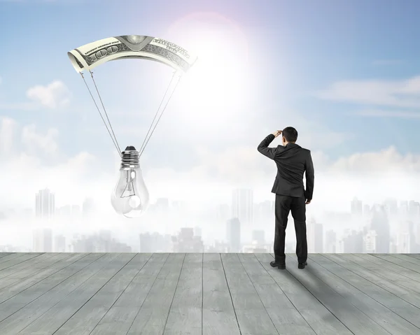 Бизнесмен смотрит на лампочку с денежным парашютом — стоковое фото