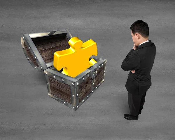 Geschäftsmann blickt auf goldenes Puzzleteil in Schatztruhe — Stockfoto