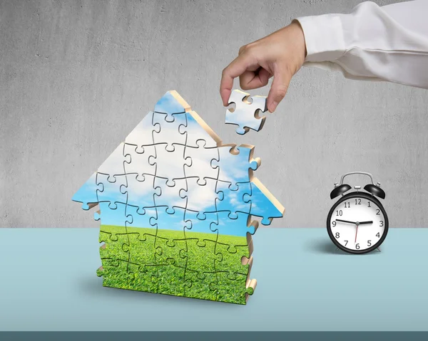 Hand holding the last piece of house puzzle with clock — Stock Photo, Image