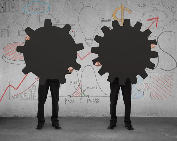 Two businessmen holding different gear with doodles wall — Stock Photo, Image