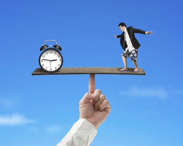 Businessman standing on finger seesaw vs clock — Stock Photo, Image