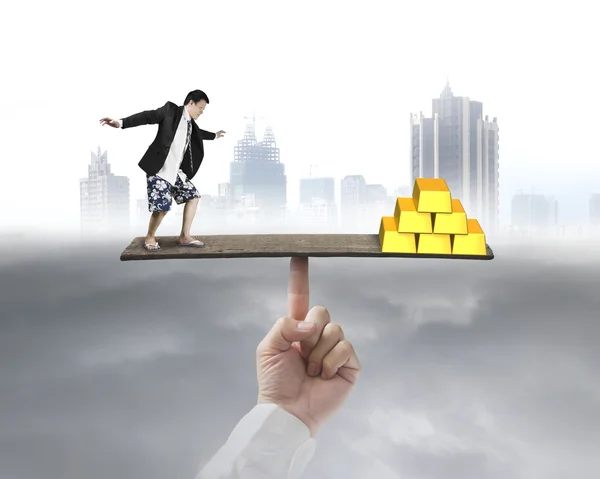 Businessman stands on finger seesaw vs gold — Stock Photo, Image