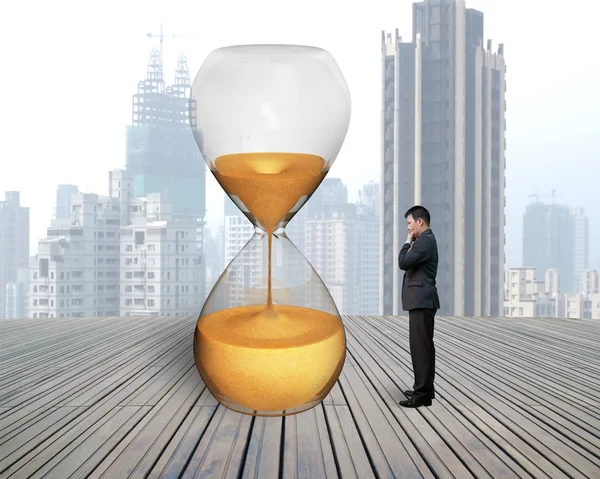 Standing businessman thinking with hourglass — Stock Photo, Image