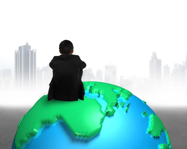 Businessman sitting on 3d map globe watching gray buildings city — Stock Photo, Image