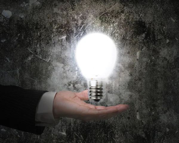 Human hand holding brightly light bulb illuminated dark old wall Royalty Free Stock Photos