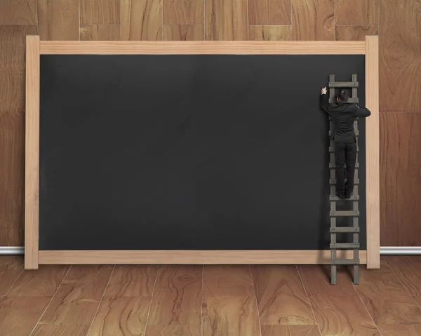 Businessman climbing ladder drawing on black blank chalkboard — Stock Photo, Image