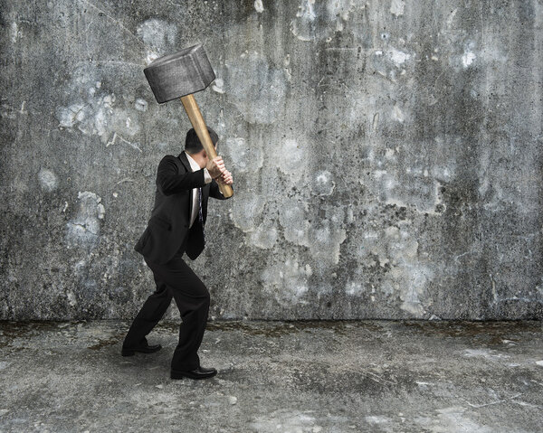 Businessman hold sledgehammer to crack old mottled concrete wall