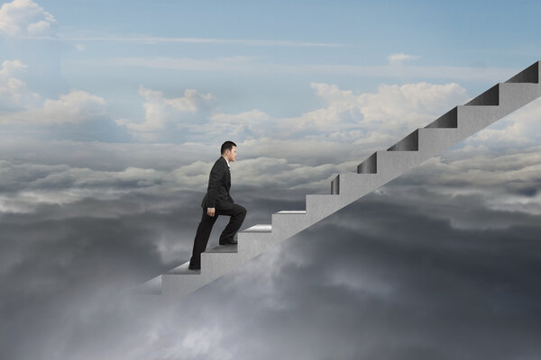 businessman climbing on concrete stairs with natural cloudy sky 