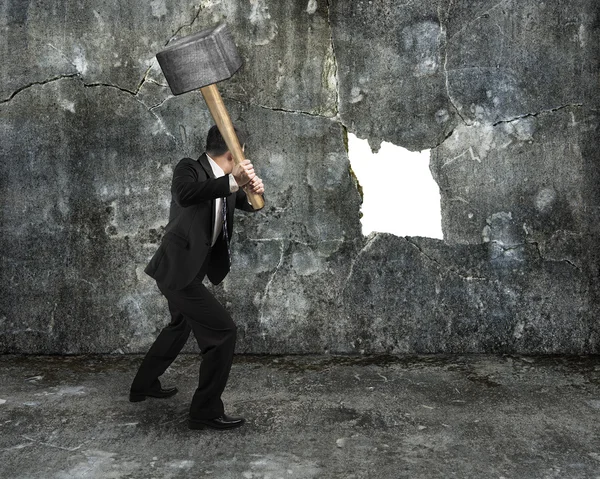 Hombre de negocios mantenga martillo agrietando gran agujero blanco en concreto — Foto de Stock