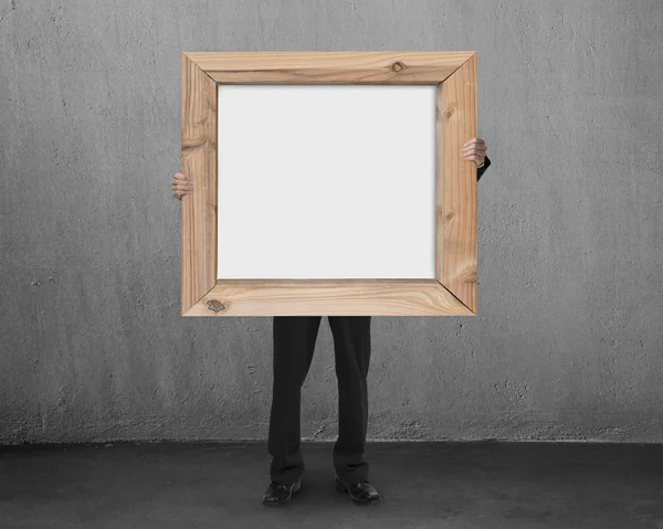 Homme tenir tableau blanc vierge avec cadre en bois dans la salle de béton — Photo