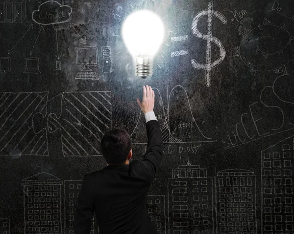 Empresário tocando brilhantemente lâmpada luminosa iluminado rabisco escuro — Fotografia de Stock