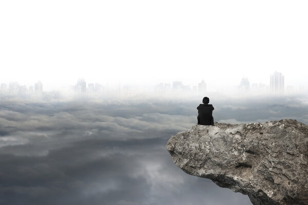 man sitting on cliff with gray cloudy sky cityscape background