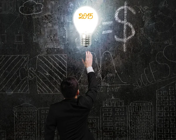 Businessman touching 2015 light bulb illuminated dark doodles wa — Stock Photo, Image