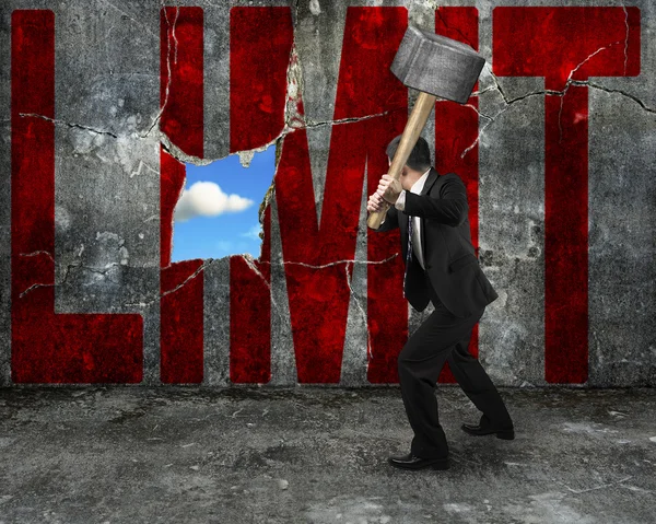 Hombre de negocios sosteniendo martillo golpeando rojo palabra LIMIT en hormigón wa — Foto de Stock
