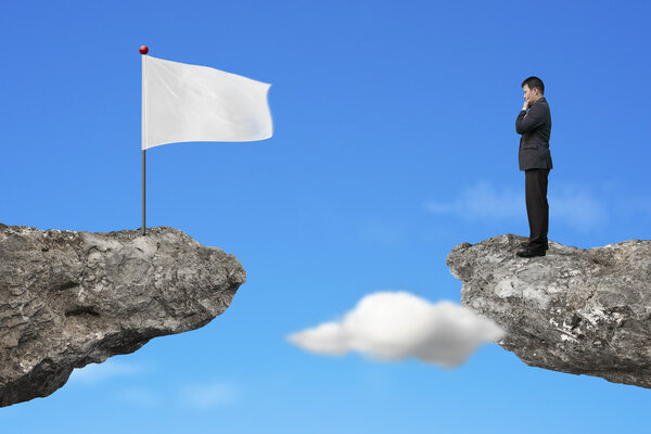 Manager standing on cliff with blank white flag and sky