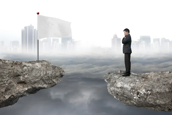 Manager standing on cliff with white flag and cloudy cityscape — Stock Photo, Image