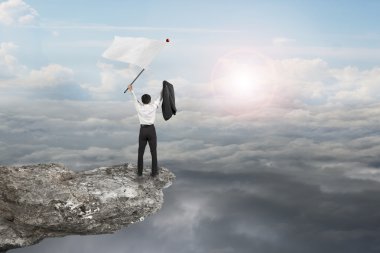 A businessman cheering on cliff waving flag with sunlight clouds