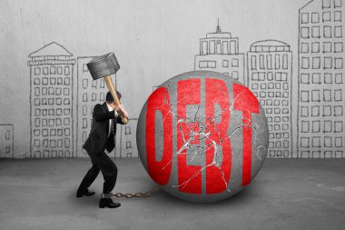 businessman holding hammer hitting cracked DEBT ball with buildi