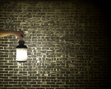 Hand holding vintage lamp illuminating dark brick wall