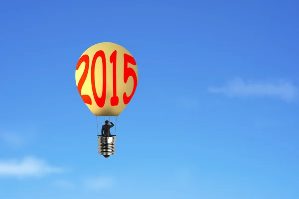 Businessman take 2015 bulb-shaped hot air balloon with blue sky — Stockfoto