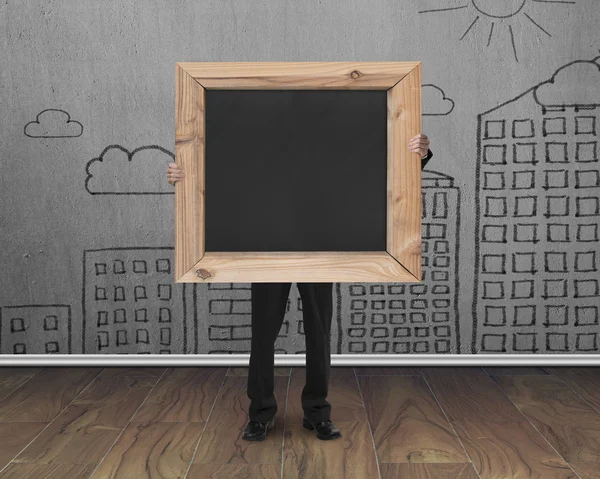 Businessman holding black blank chalkboard with cityscape doodle — Zdjęcie stockowe