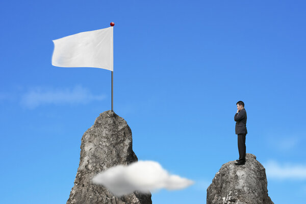 Businessman standing on peak with blank white flag and sky