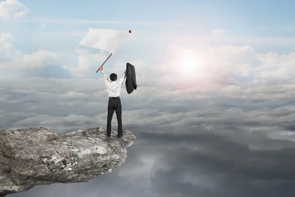 A businessman cheering on cliff waving flag with sunlight clouds — Stock fotografie