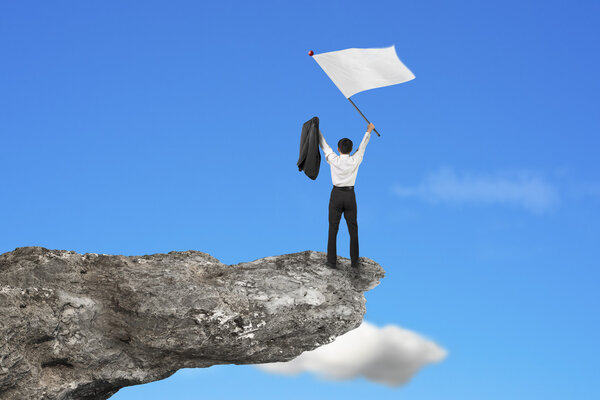 A businessman cheering on cliff waving blank flag with sky