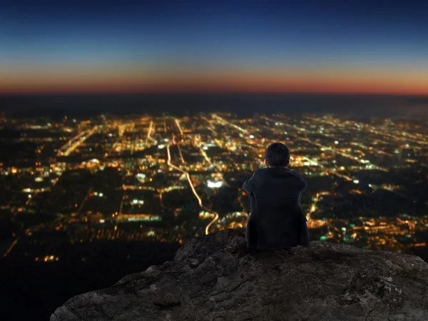 Empresário sentado na montanha rochosa com vista noturna da cidade — Fotografia de Stock