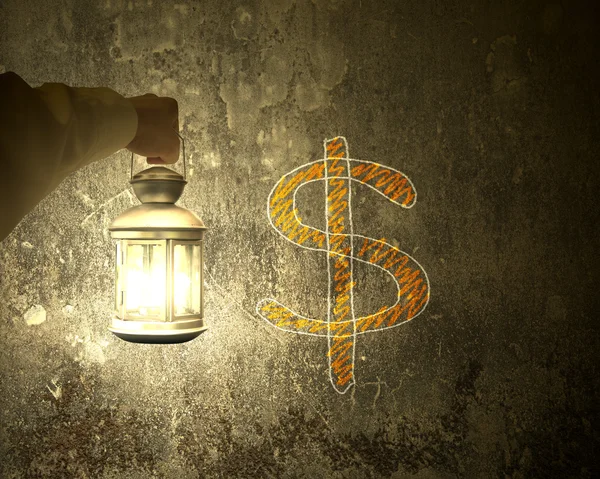 Hand holding vintage lamp illuminating dollar sign on dark wall — Stok fotoğraf