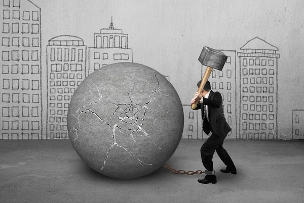 businessman holding hammer hitting cracked concrete ball with bu