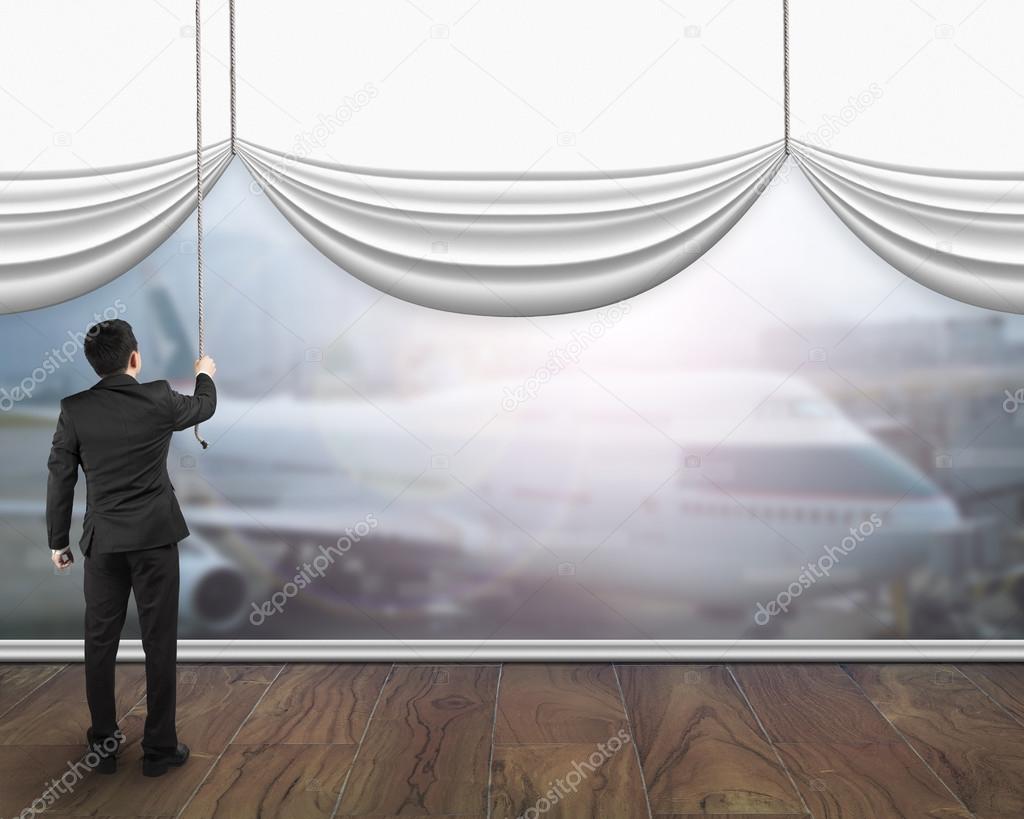 A businessman pulling open white blank curtain showing airplane 