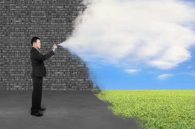 Businessman spraying clouds sky grass paint cover old brick wall