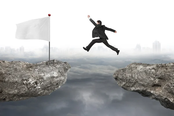 Бізнесмен стрибає на скелі з білим прапором і хмарним міським пейзажем — стокове фото