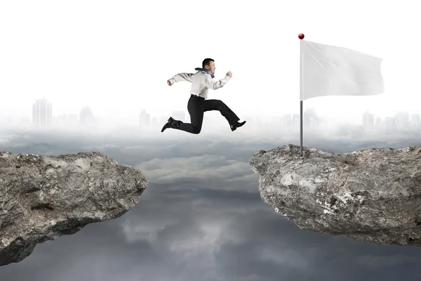 Man jumping on cliff with white flag and cloudy cityscape — 스톡 사진