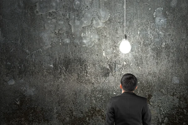 Businessman looking at brightly light bulb illuminated dark conc — Stock Photo, Image