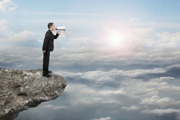 Businessman using megaphone yelling on cliff with sunlight cloud — Zdjęcie stockowe