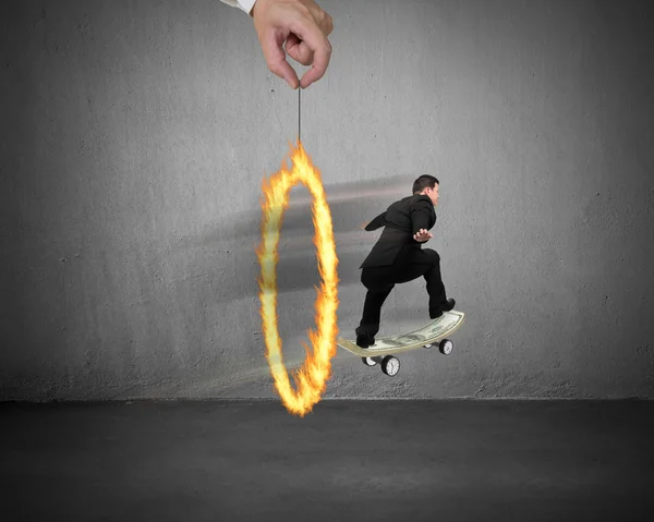 Businessman skating on money skateboard through fire circle — Stock Photo, Image