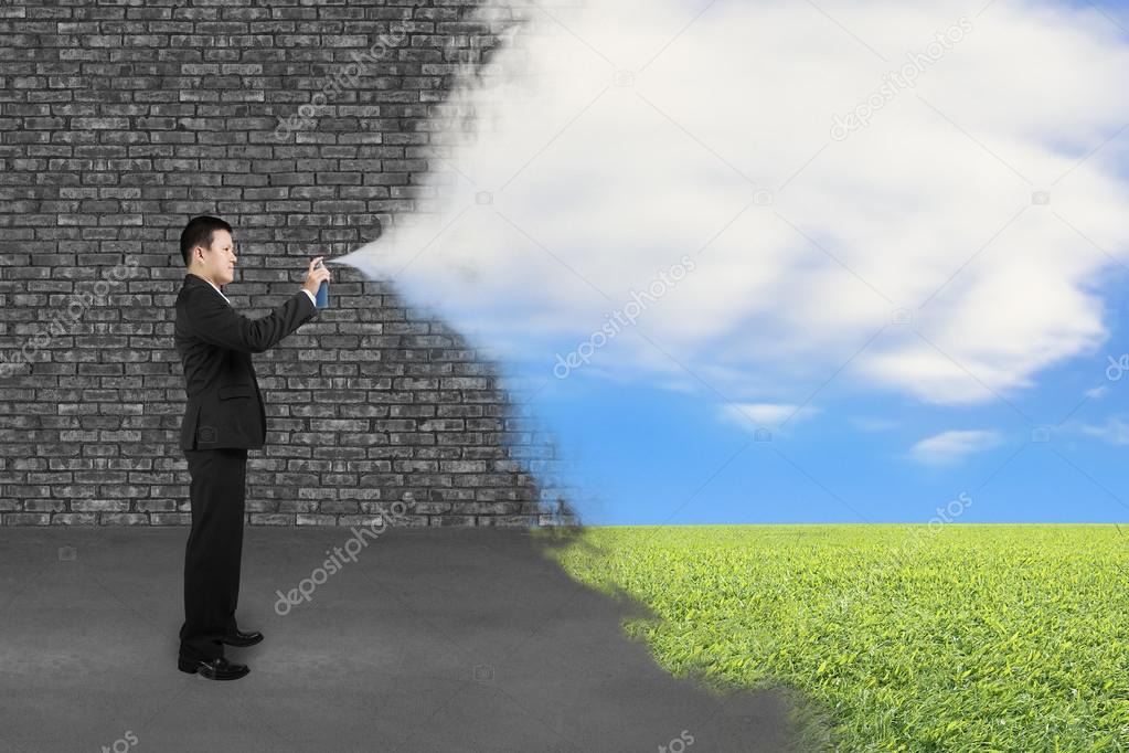 Businessman spraying clouds sky grass paint cover old brick wall