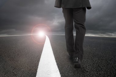 Businessman walking on asphalt road with sunlight cloudy sky
