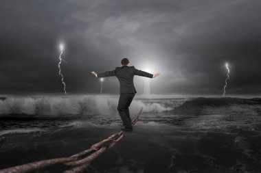 Businessman balancing on old iron chain with dark stormy ocean