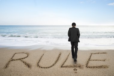 Rear view businessman standing with rule word on sand beach