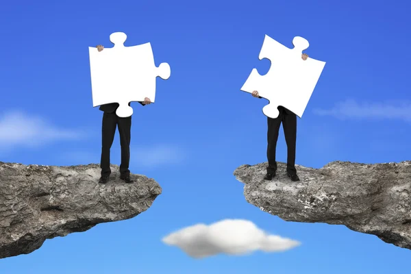 Businessmen holding jigsaw puzzles to connect on cliff with sky — Stok fotoğraf